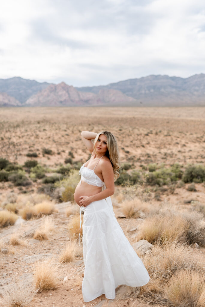 Wide maternity portrait in white skirt set with desert and mountains at Red Rock Canyon