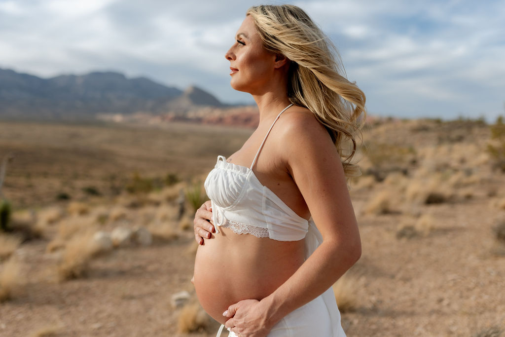 Close up maternity photo of baby bump in white outfit at golden hour in the desert