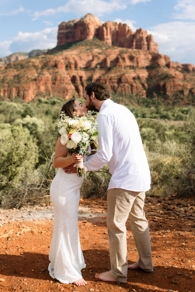 Couple kissing during Sedona elopement with red rock mountains behind