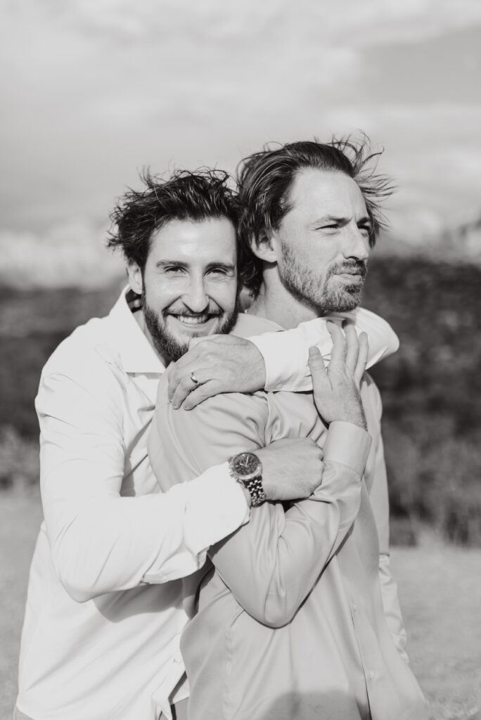 Black and white portrait of two men hugging with windblown hair outdoors