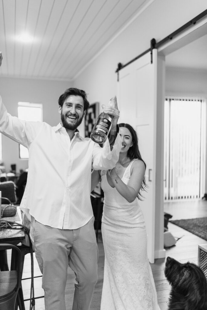 Black and white photo of couple celebrating indoors with champagne before elopement