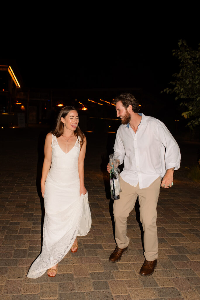 Newlywed couple walking together at night after their elopement, laughing and holding drinks