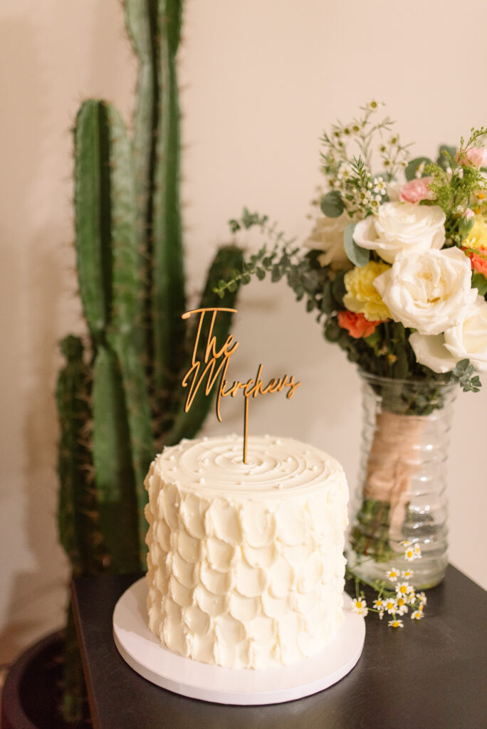 Small white celebration cake with floral arrangement and cactus in the background