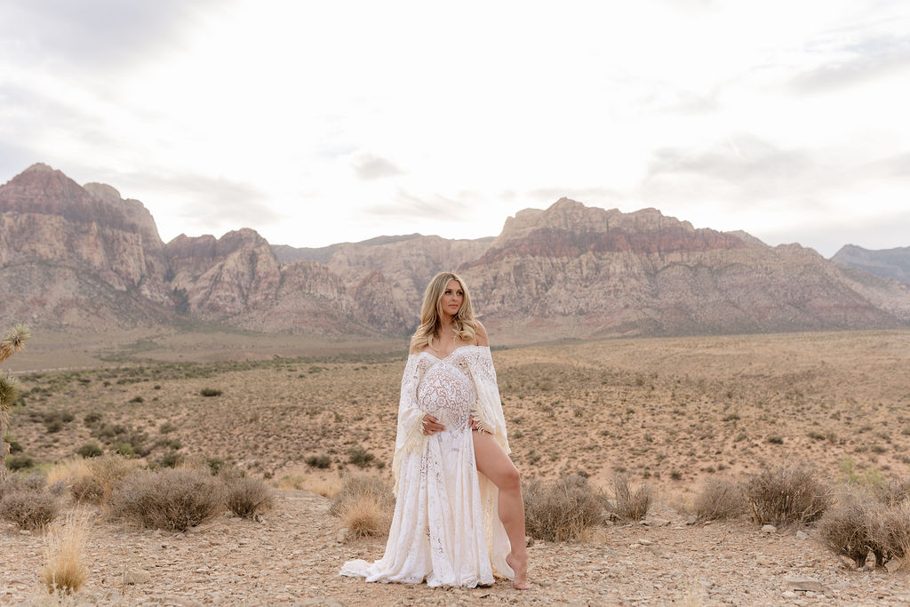 Full length maternity portrait in white lace dress with mountains at Red Rock Canyon