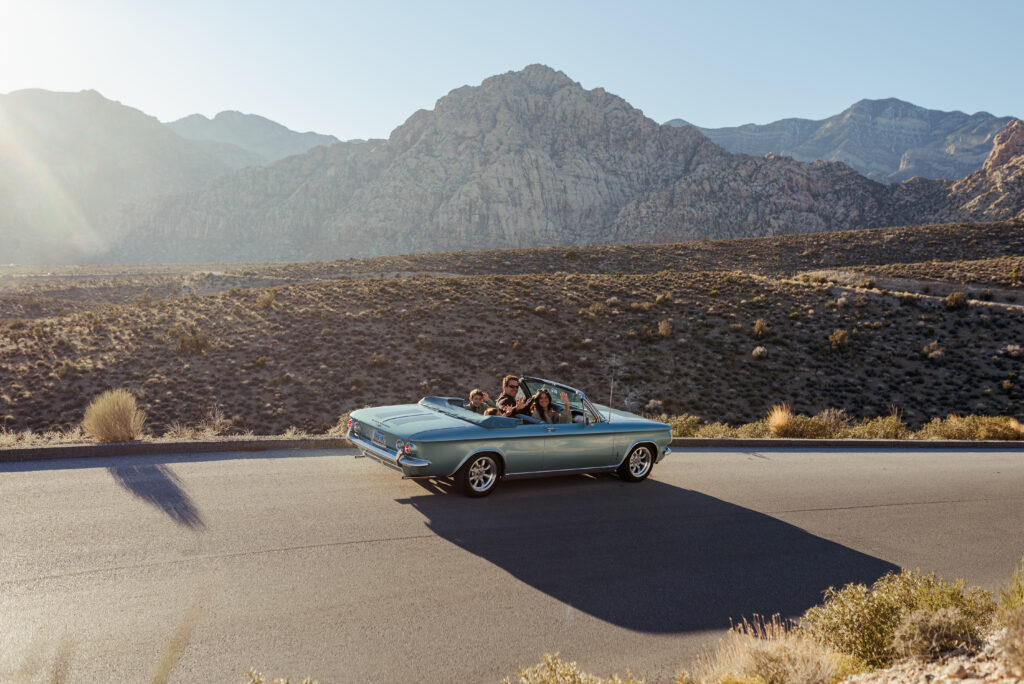 Blue vintage convertible parked on the Red Rock Scenic Loop with mountains in the background.