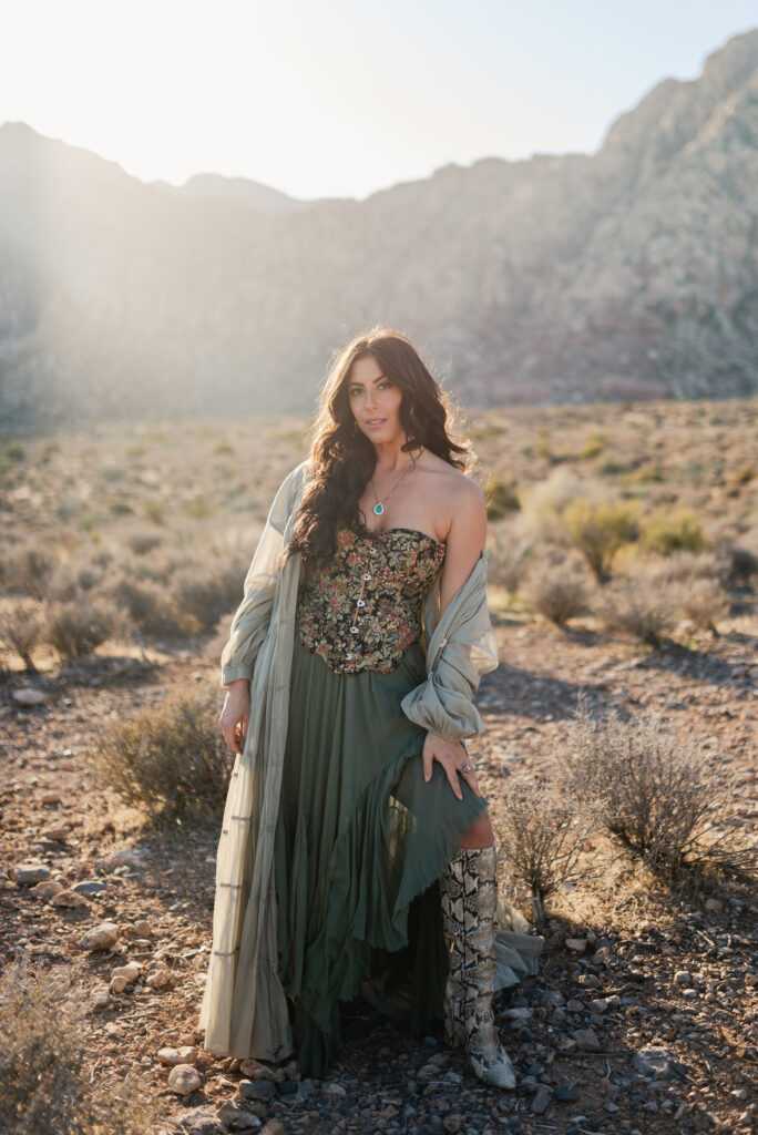 Woman in a green dress standing in desert light near Red Rock Canyon at golden hour.
