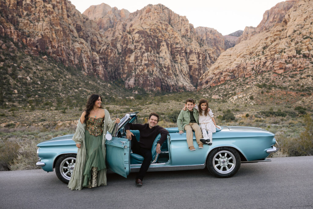 Family posing around a blue vintage convertible on the Red Rock Scenic Loop at sunset.