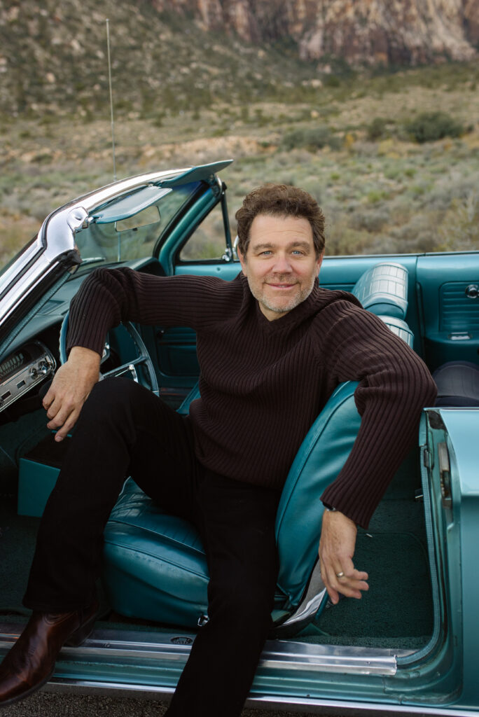 Man sitting in the driver’s seat of a blue vintage convertible during a lifestyle family session.