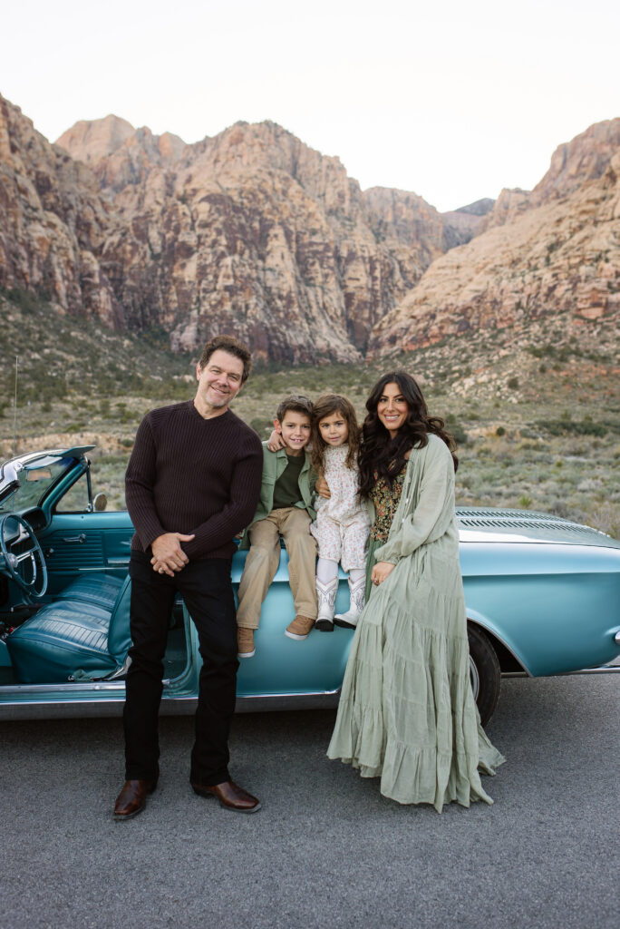 Family portrait beside a blue vintage convertible on the Red Rock Scenic Loop at sunset.