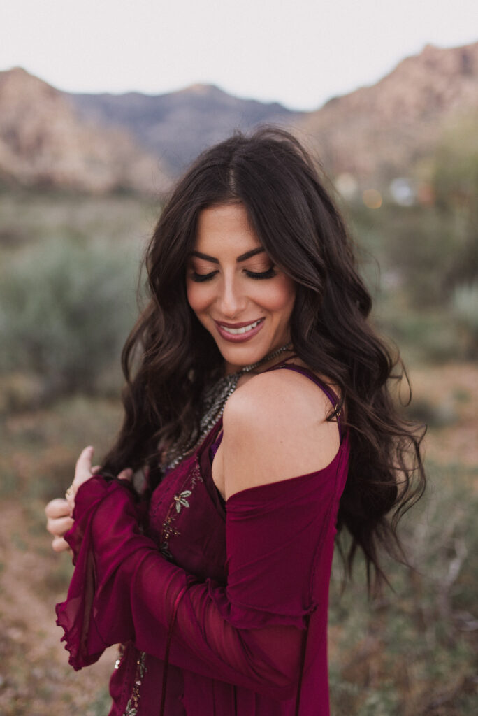 Woman in a burgundy dress smiling during golden hour portraits in the Las Vegas desert.